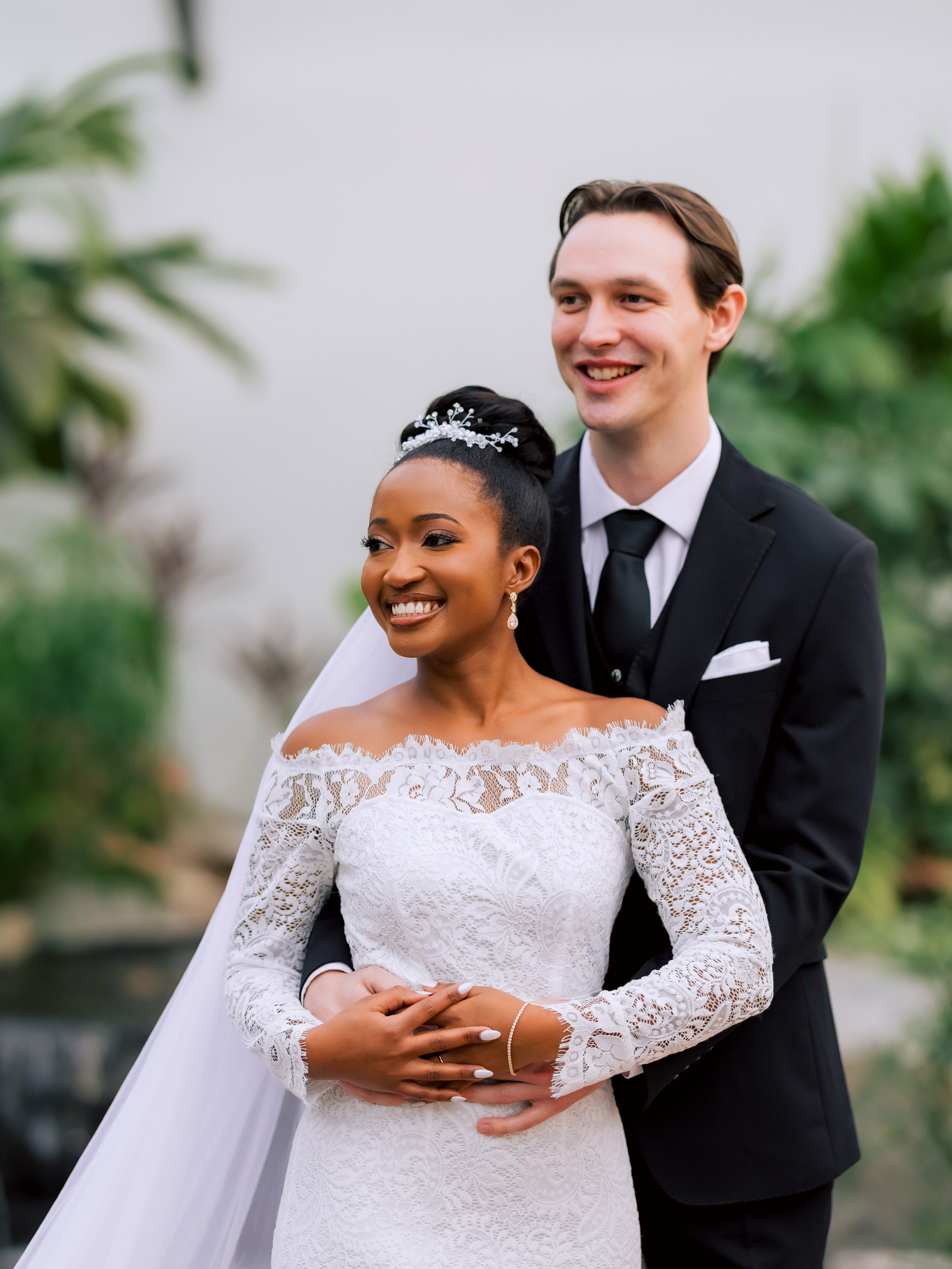 A smiling bride and groom embrace in front of green foliage.