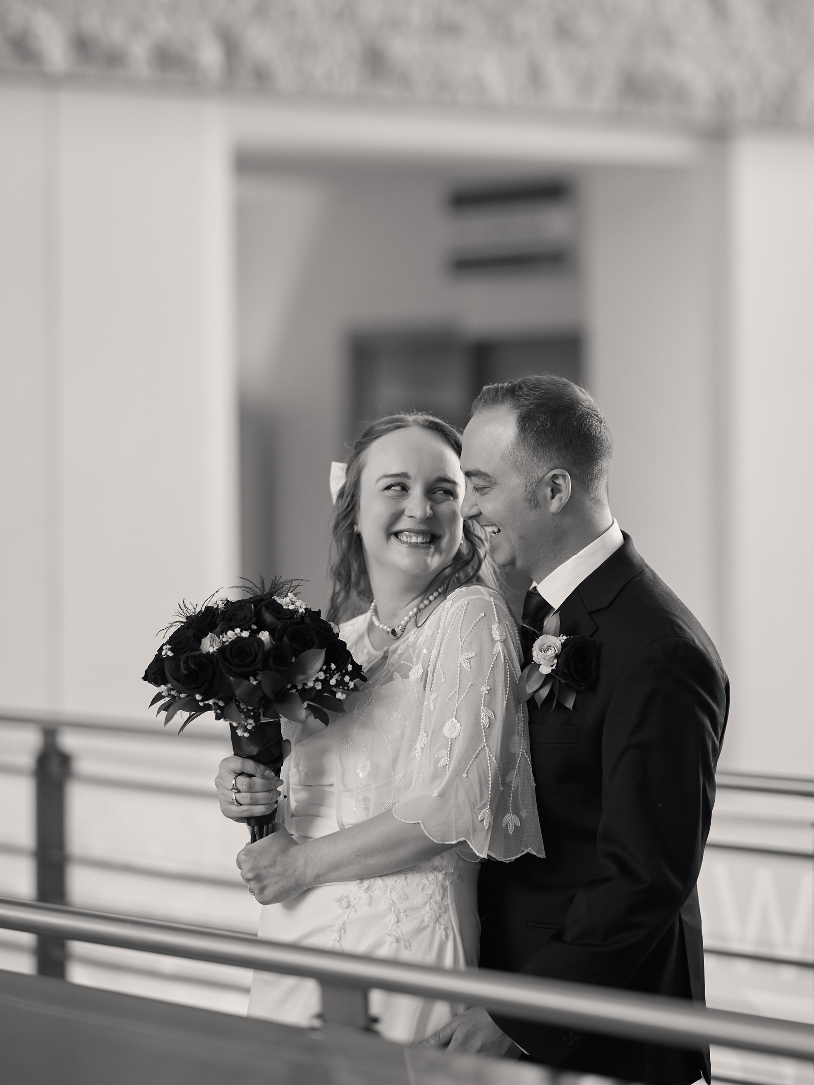 Black-and-white portrait of a smiling couple beside a railing.